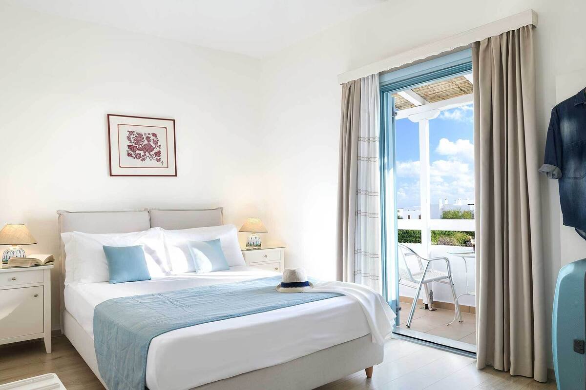 A hotel room with a bed, nightstands, a framed picture, and a view of the outdoors.