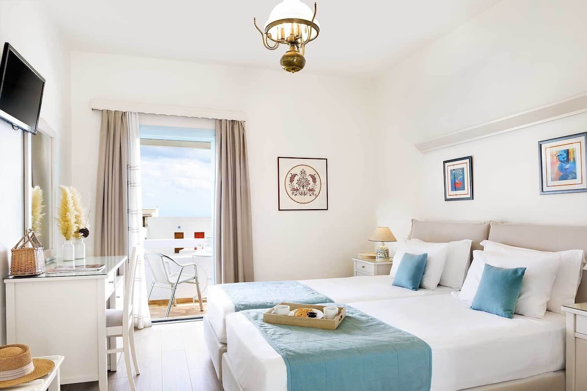 A hotel room with two beds, a desk, a chair, a TV, and artwork on the walls.
