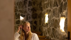 A person sitting on a wooden bench in a stone-walled room with two wall-mounted lights. - Heybe Hotel & Spa (Nevsehir)