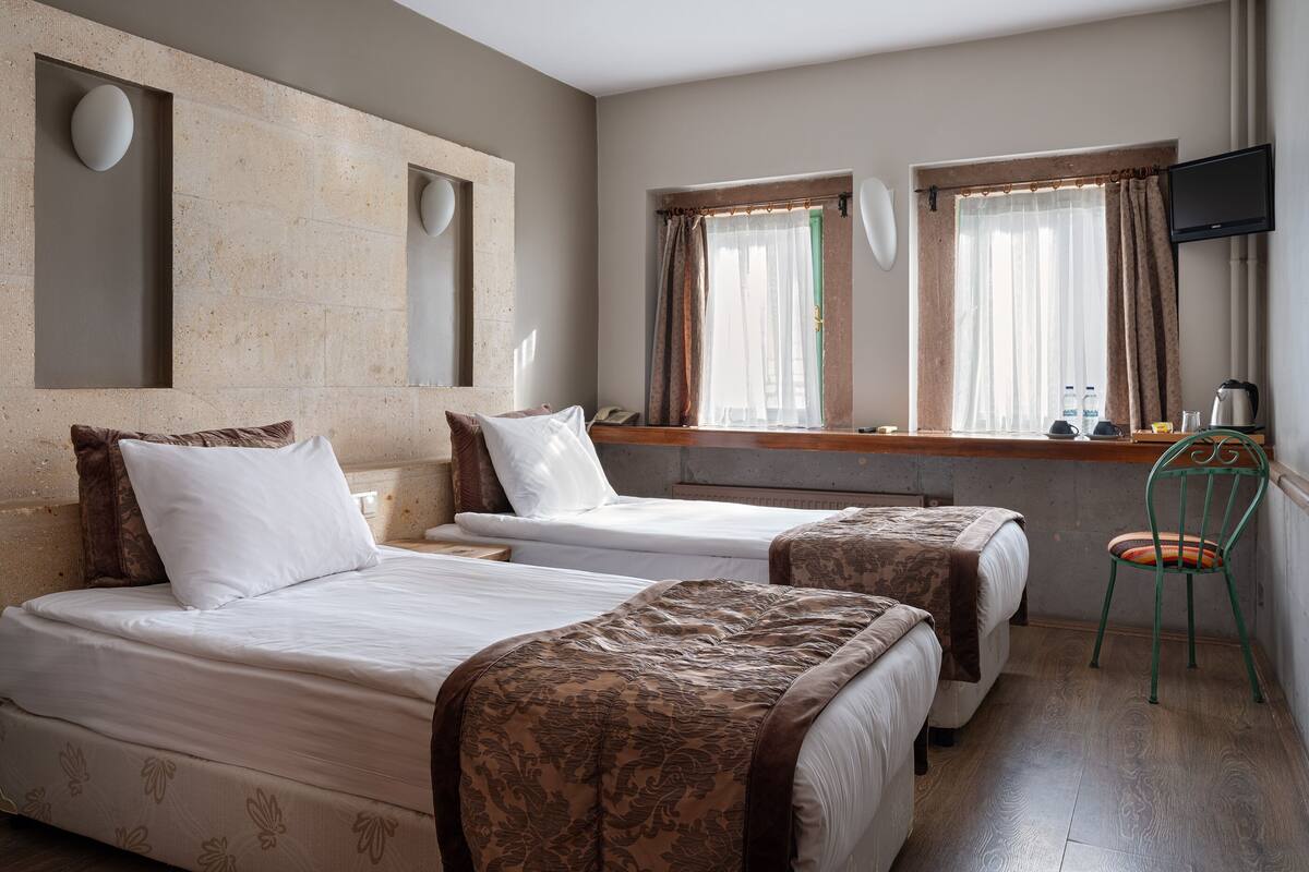 A hotel room with two beds, a TV, a window with curtains, and a chair.