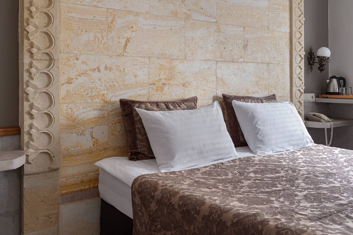 A bedroom with a stone headboard, a bed with a patterned bedspread, and a bedside table with a lamp.