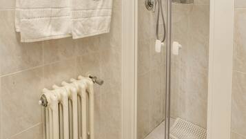 A bathroom with a glass shower enclosure, a white radiator, and two white towels hanging on the wall.