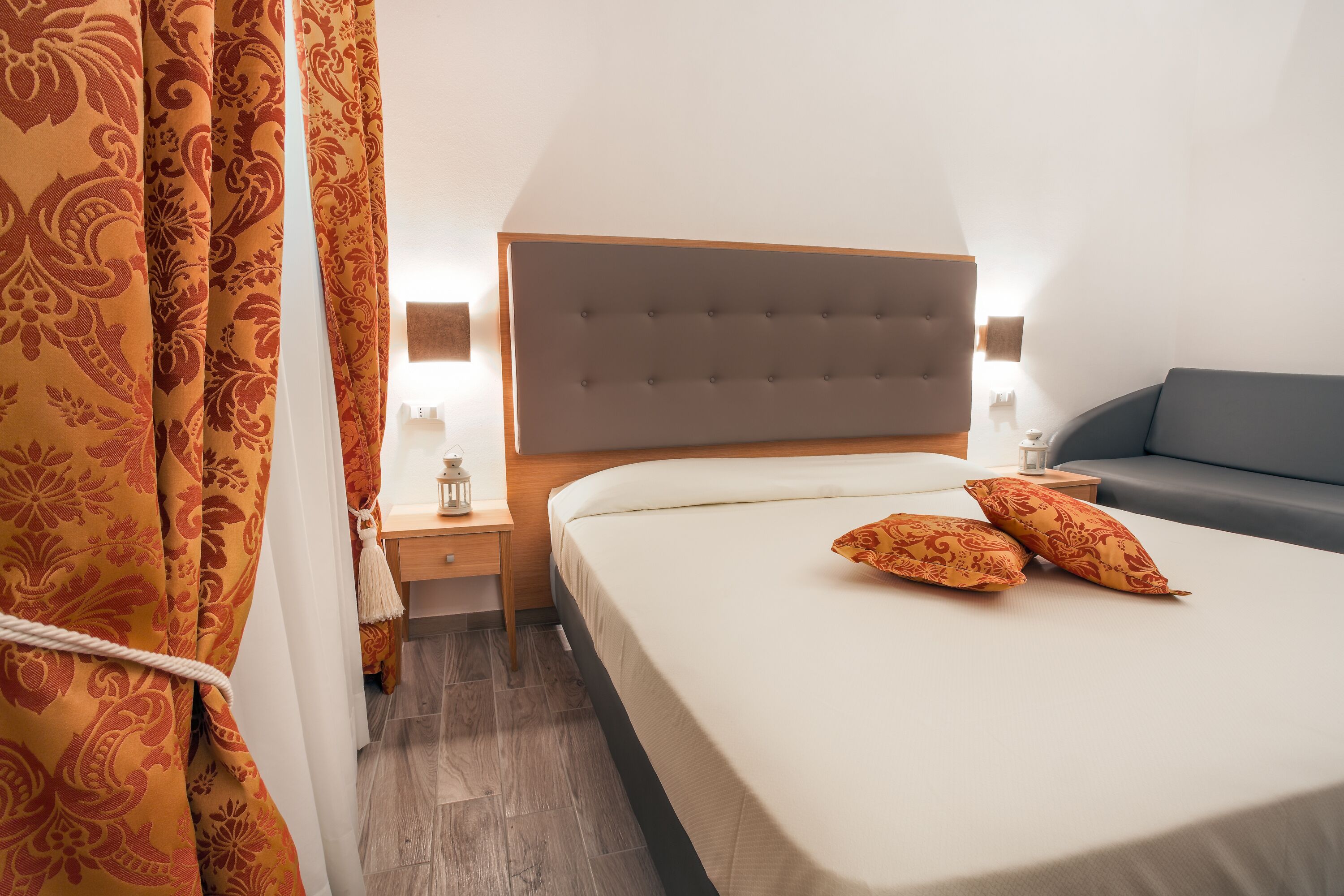 A hotel room with a large bed, a nightstand, a lamp, and a sofa.
