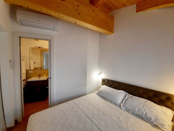 A bedroom with a bed, a nightstand, a wall-mounted light, and an air conditioning unit.