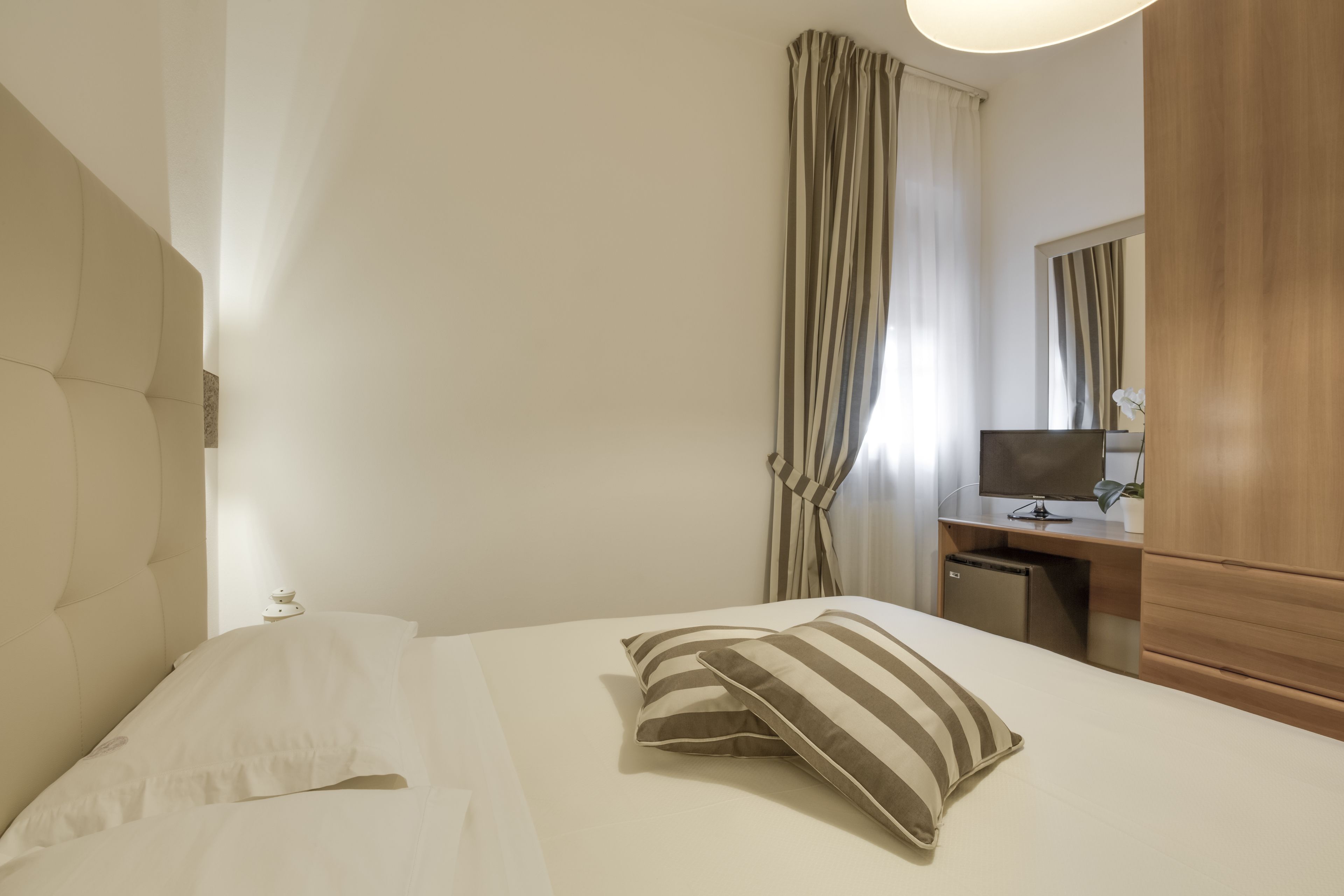 Una habitación de hotel con una cama, un escritorio con una computadora y un espejo.
