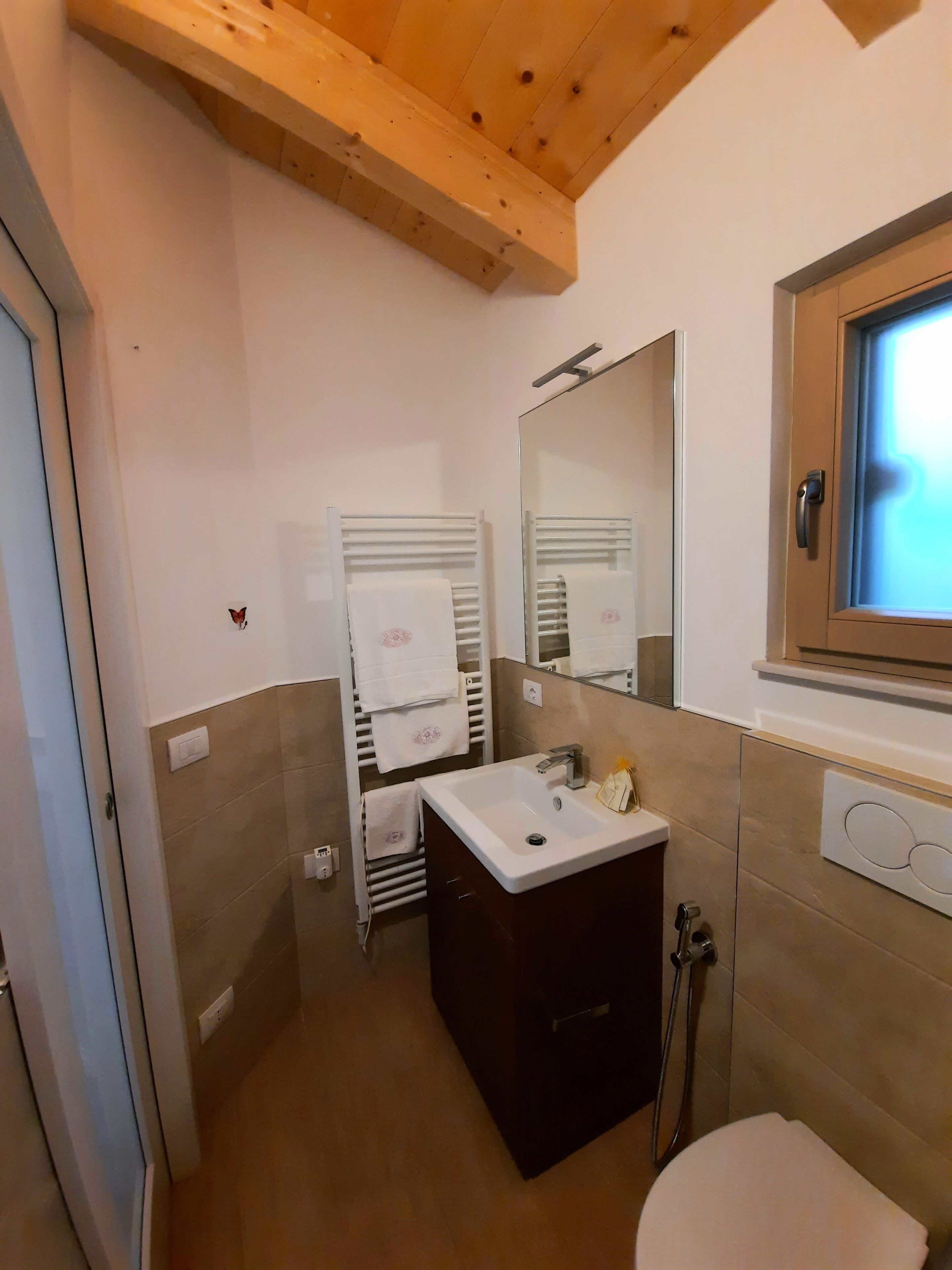 Ein kleines Badezimmer mit Holzboden, einem weißen Waschbecken, einem Spiegel und einer Toilette.