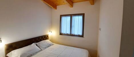 A bedroom with a wooden ceiling, a single bed with white bedding, a nightstand, and a window with curtains.