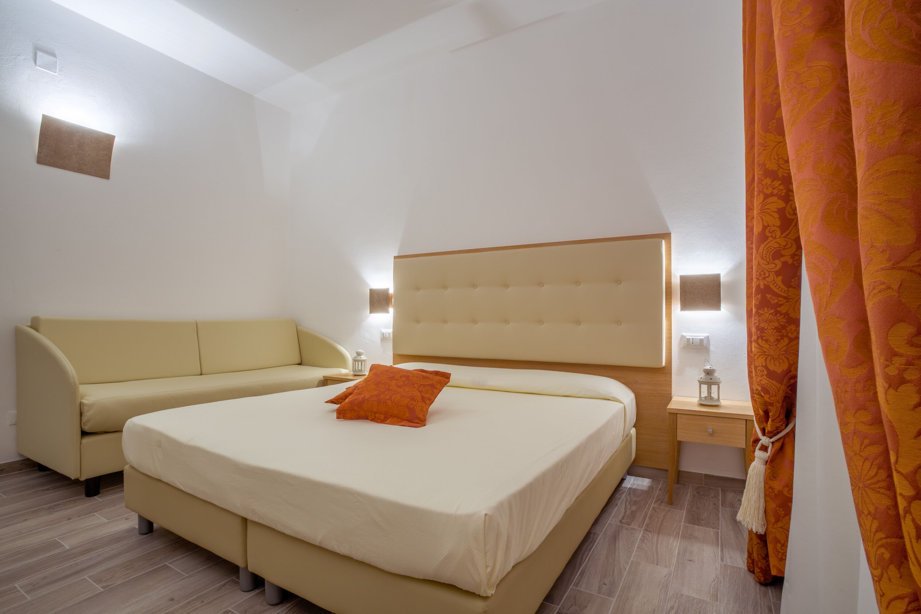 A bedroom with a large bed, a sofa, a bedside table, and a nightstand.