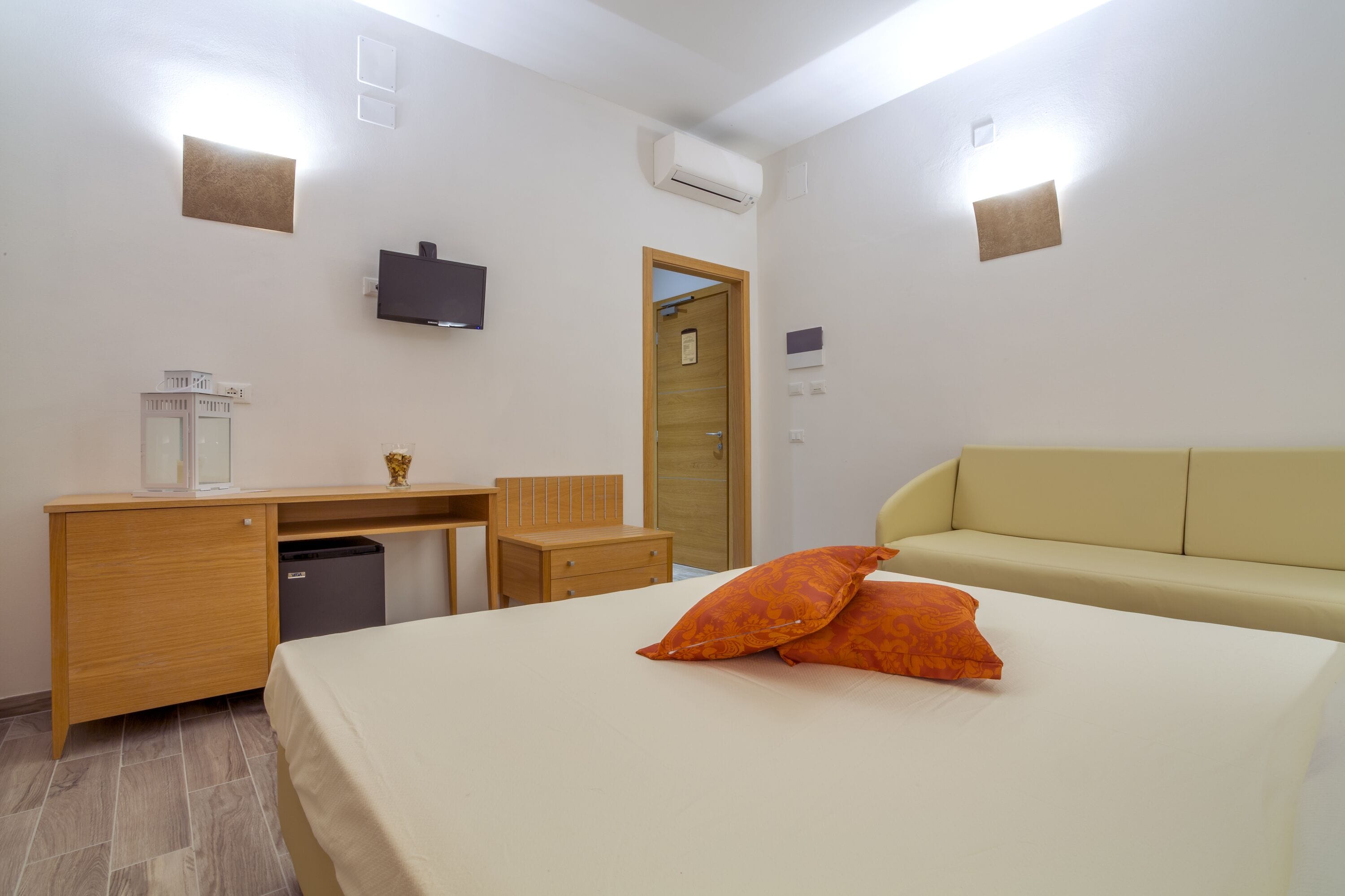 Una habitación de hotel con cama, escritorio, armario y un pequeño cubo de basura.