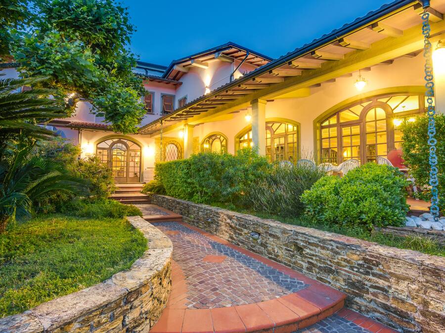 A well-lit, stone-walled pathway leading to a building with arched windows and a covered porch.