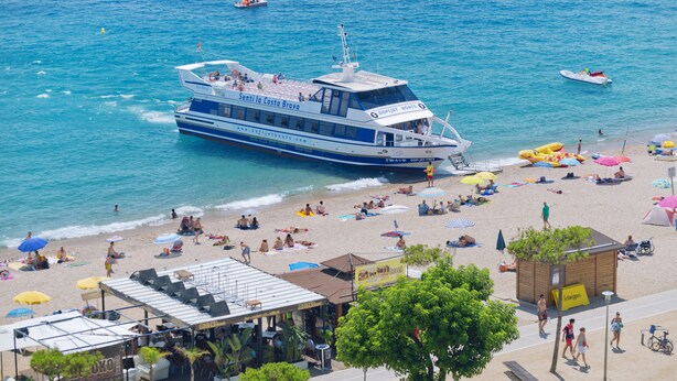Une plage avec un grand bateau, des parasols et des gens qui se détendent.