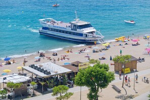 Een strand met een groot schip, parasols en mensen die ontspannen.