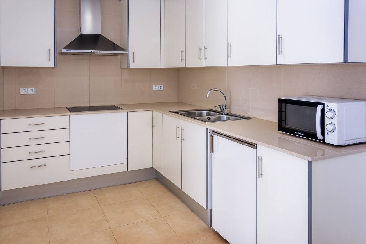 A modern kitchen with white cabinets, a stainless steel sink, and a built-in microwave.