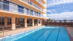 Une piscine à l’eau d’un bleu cristallin, un immeuble à plusieurs étages doté de balcons et une clôture en bois.