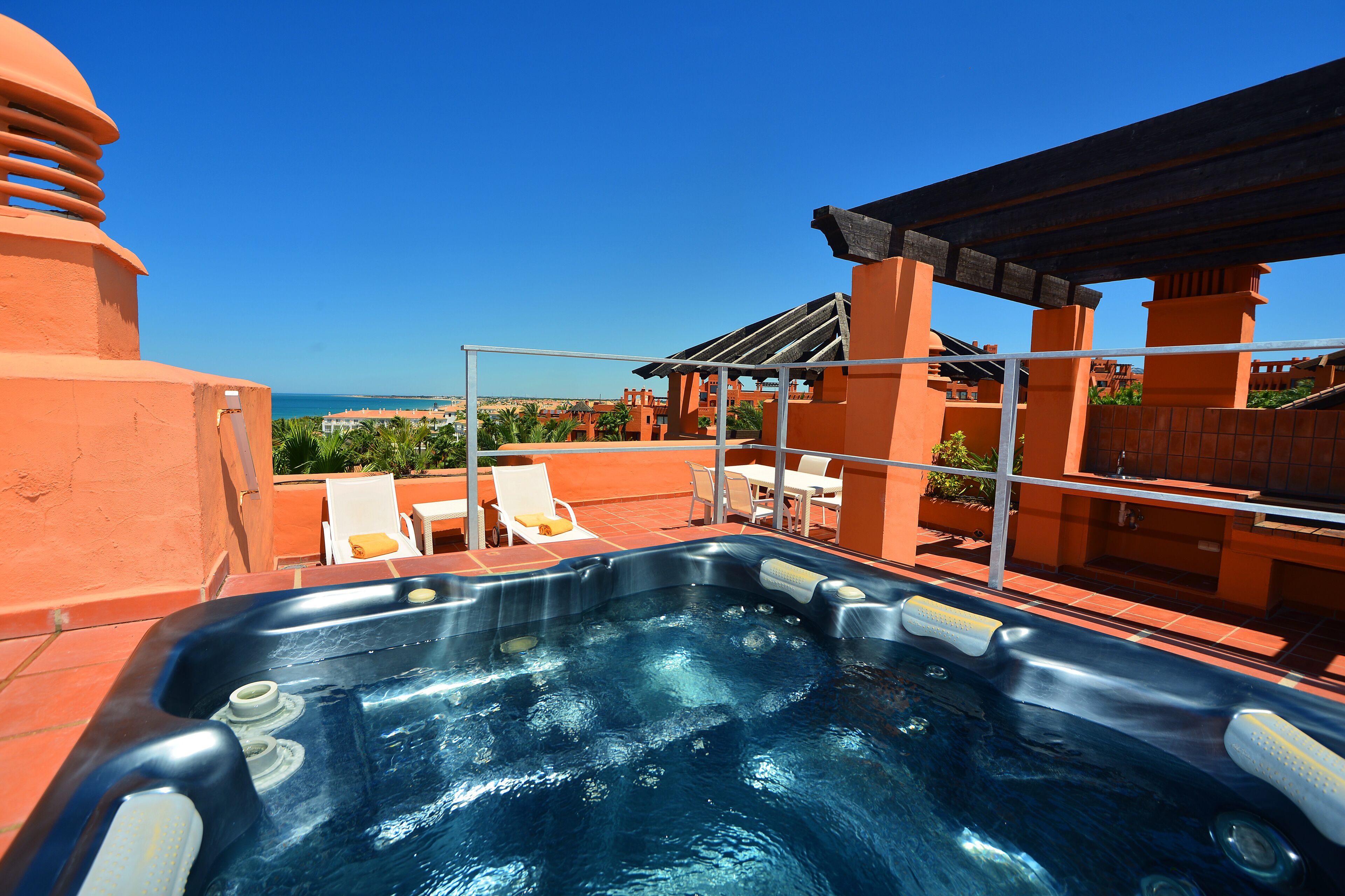 Un bain à remous avec une vue dégagée sur la mer et un espace extérieur aménagé avec des chaises et une table.