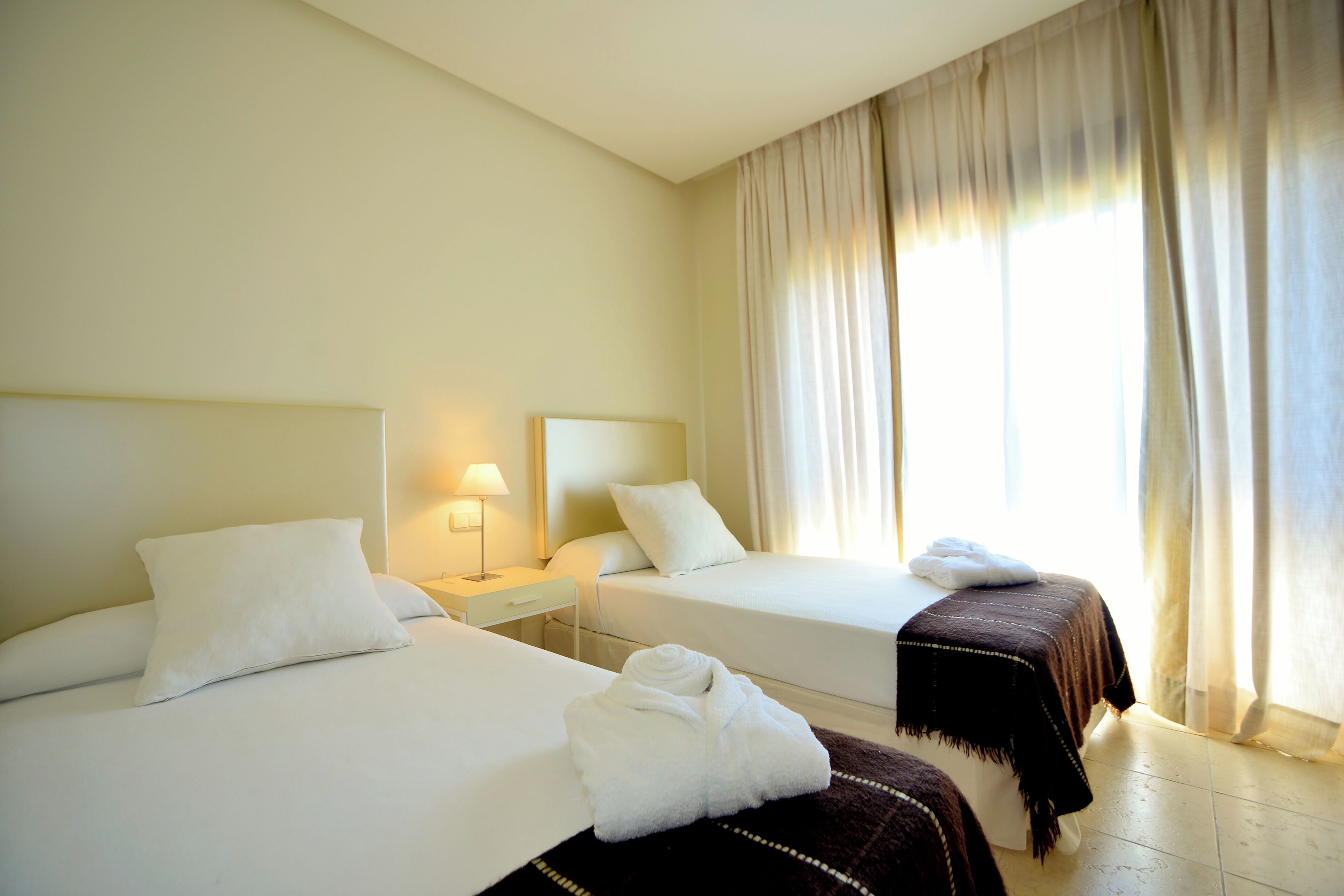 Ein Hotelzimmer mit zwei Betten, einem Nachttisch mit Lampe und einem Fenster mit Vorhängen.