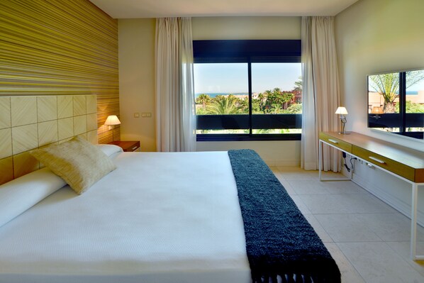 Habitación de hotel con cama, escritorio, lámpara, vistas al exterior y una ventana con cortinas.