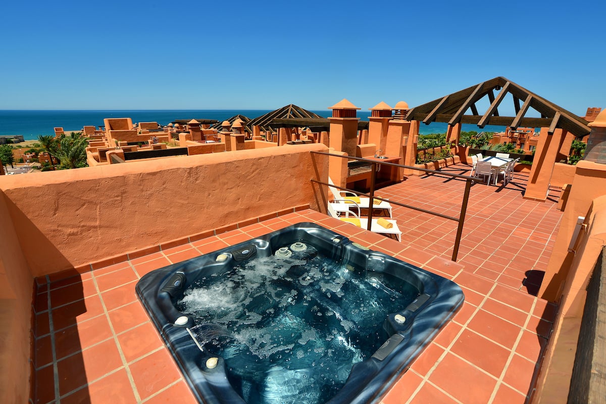 A rooftop with a hot tub, outdoor seating, and a view of the ocean.