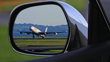 A car's side mirror reflecting an airplane on the runway.