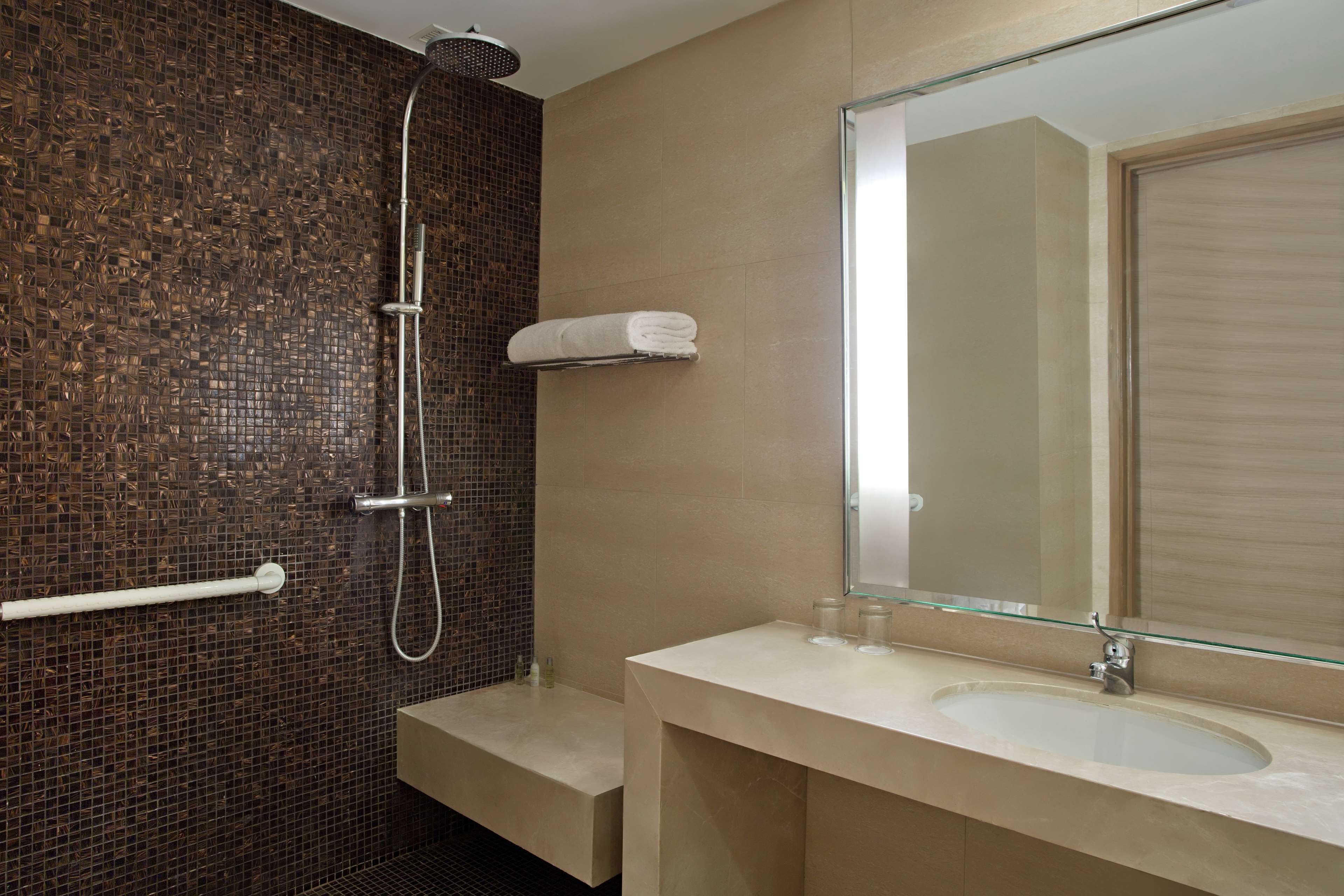 A modern bathroom with a glass shower enclosure, a beige sink, and a large mirror.