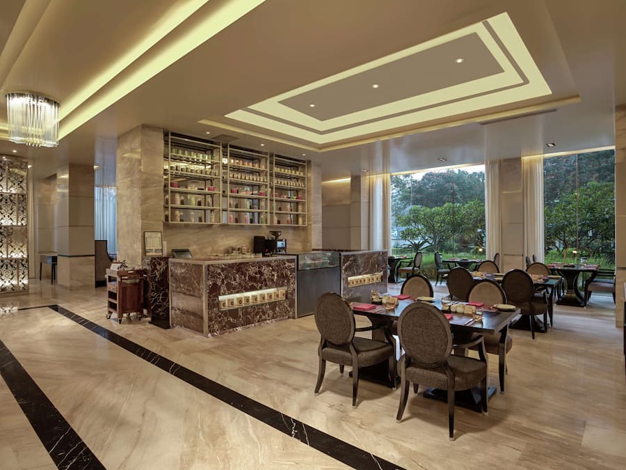 Un vestíbulo amplio con piso de mármol, un mostrador de recepción, una zona de bar con estantes y un comedor con mesas y sillas.