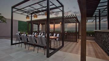 A rooftop terrace with a wooden pergola, outdoor seating, and a view of the sunset.