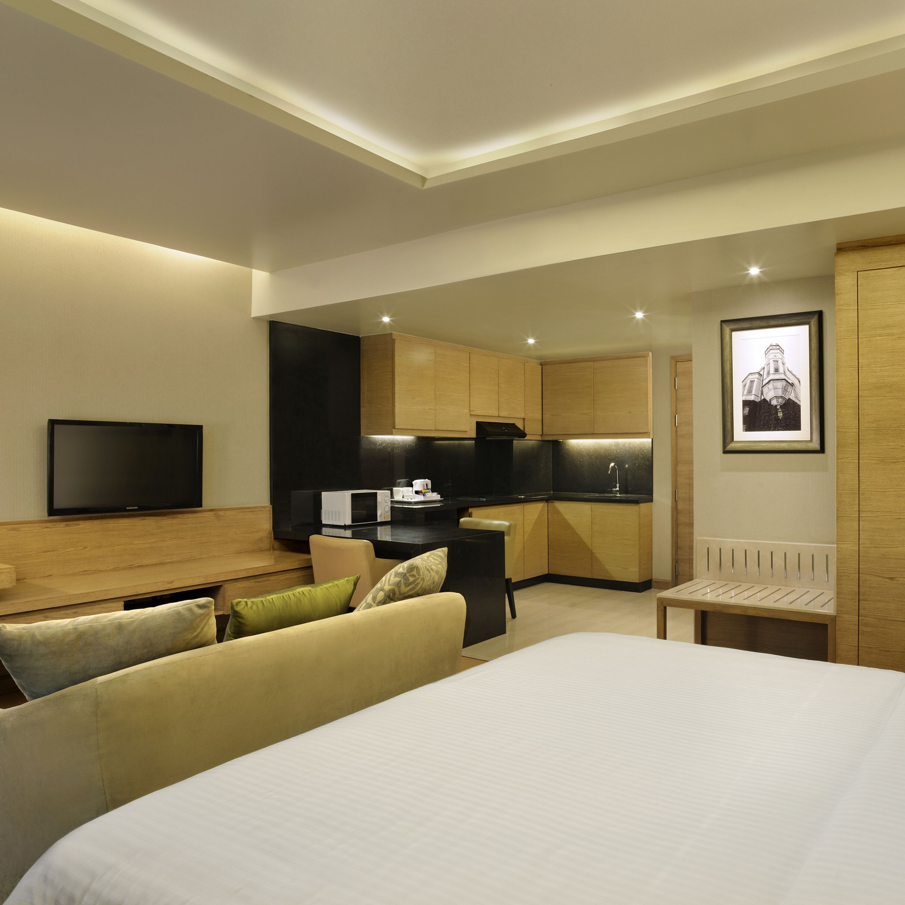 Une chambre d’hôtel moderne dotée d’un grand lit, d’un téléviseur à écran plat, d’une kitchenette et d’un tableau encadré au mur.