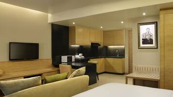 A modern hotel room with a large bed, a flat-screen TV, a kitchenette, and a framed picture on the wall.