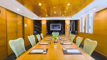 A conference room with a long table, chairs, a plant, and a TV screen.