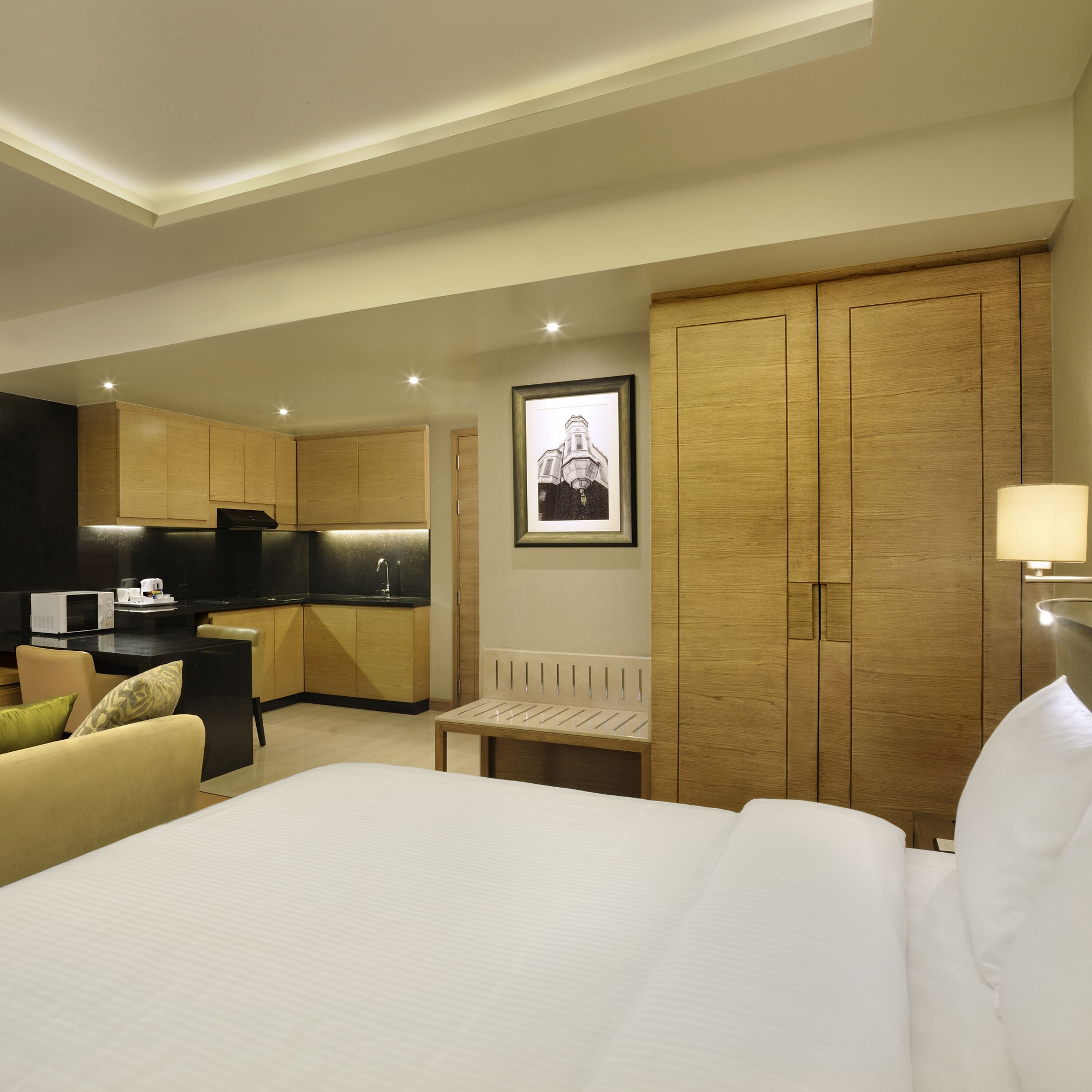 A hotel room with a bed, a desk, a chair, a kitchenette, and a wardrobe.