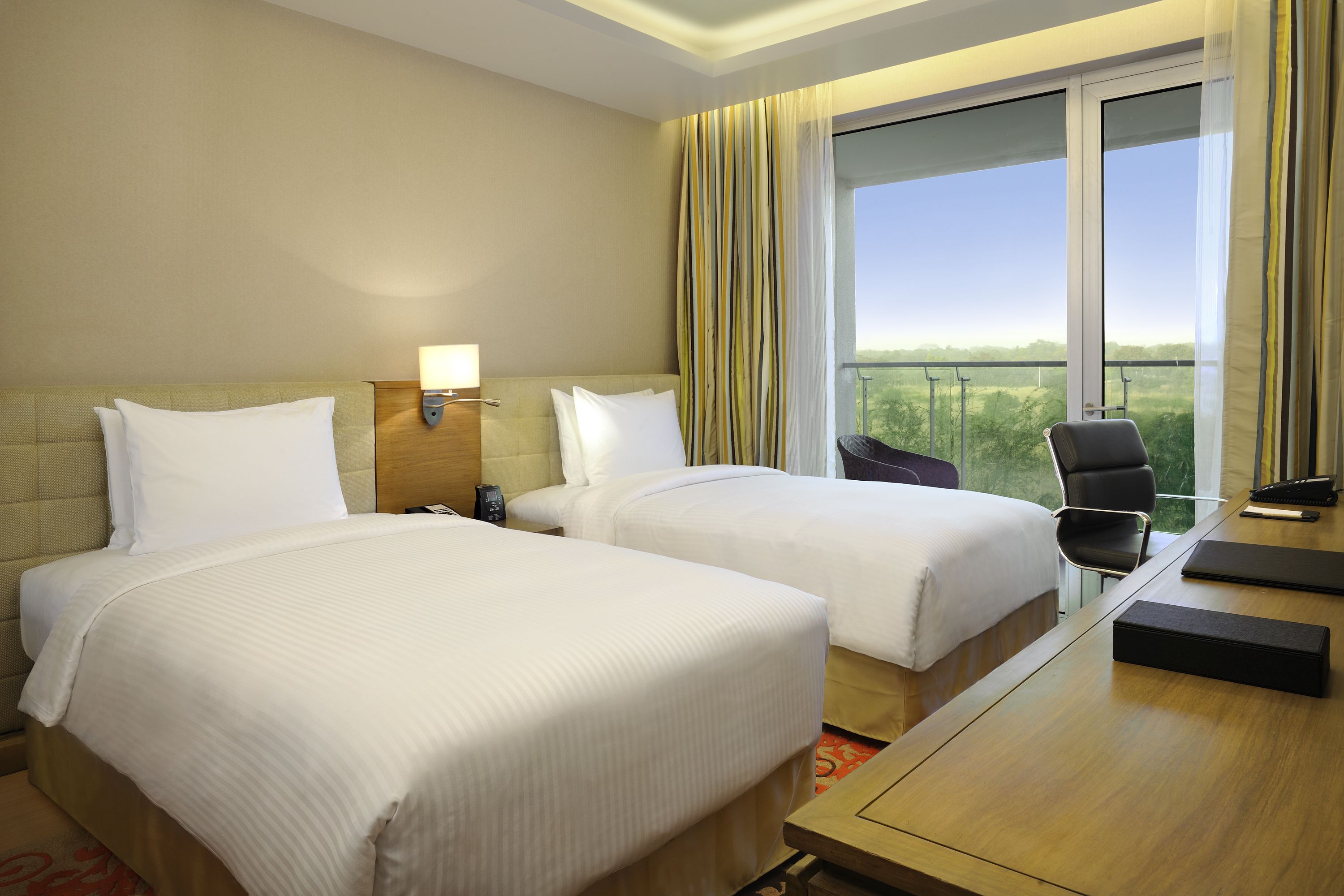 A hotel room with two beds, a desk, a chair, and a large window with curtains.