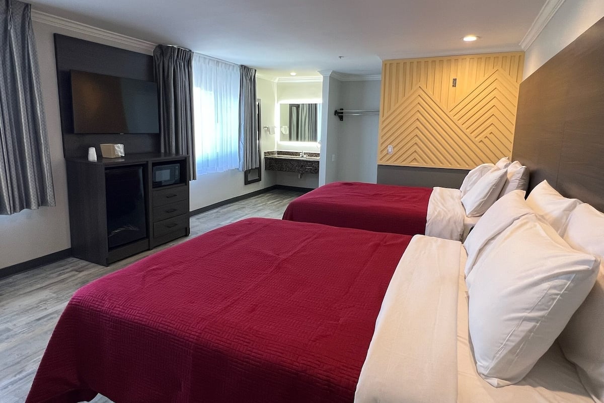 A hotel room with two beds, a TV, a dresser, a mirror, and a wooden accent wall.
