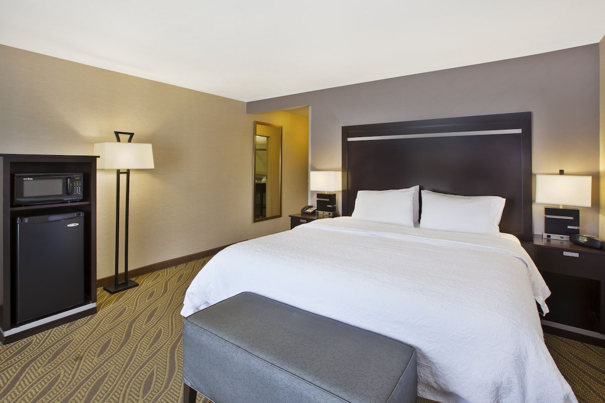 A hotel room with a bed, a desk, a lamp, a microwave, and a small refrigerator.