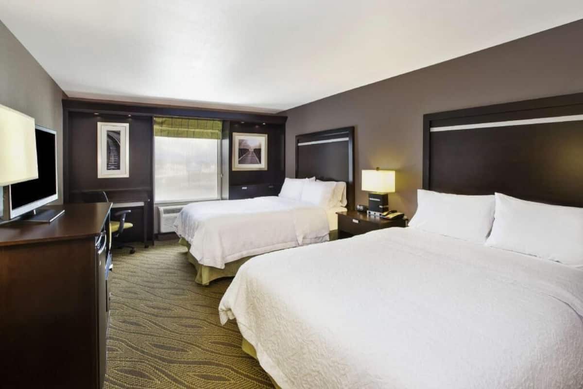 A hotel room with two beds, a desk, a TV, and a window with a view.
