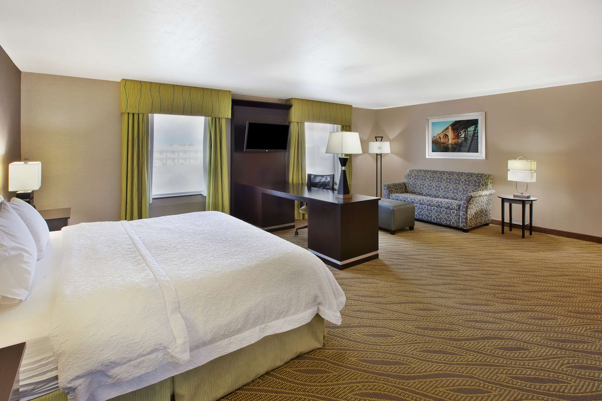 A hotel room with a large bed, a desk, a chair, and a television.