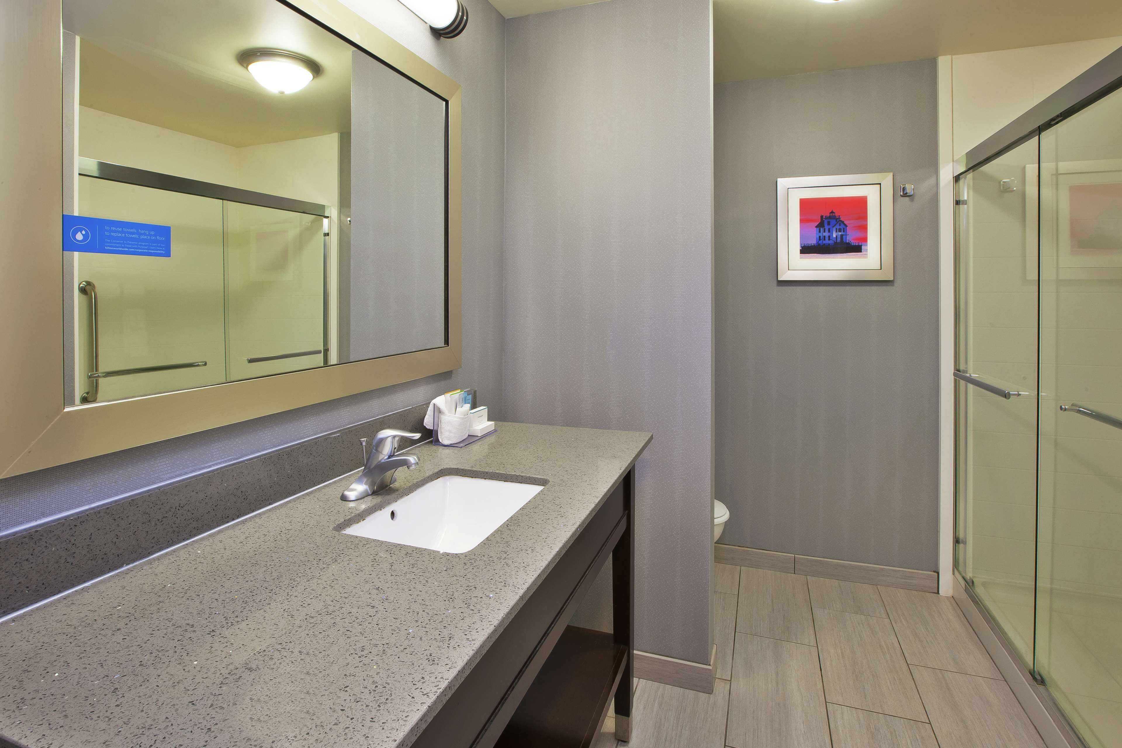 A modern bathroom with a granite countertop sink, a large mirror, and a framed picture on the wall.