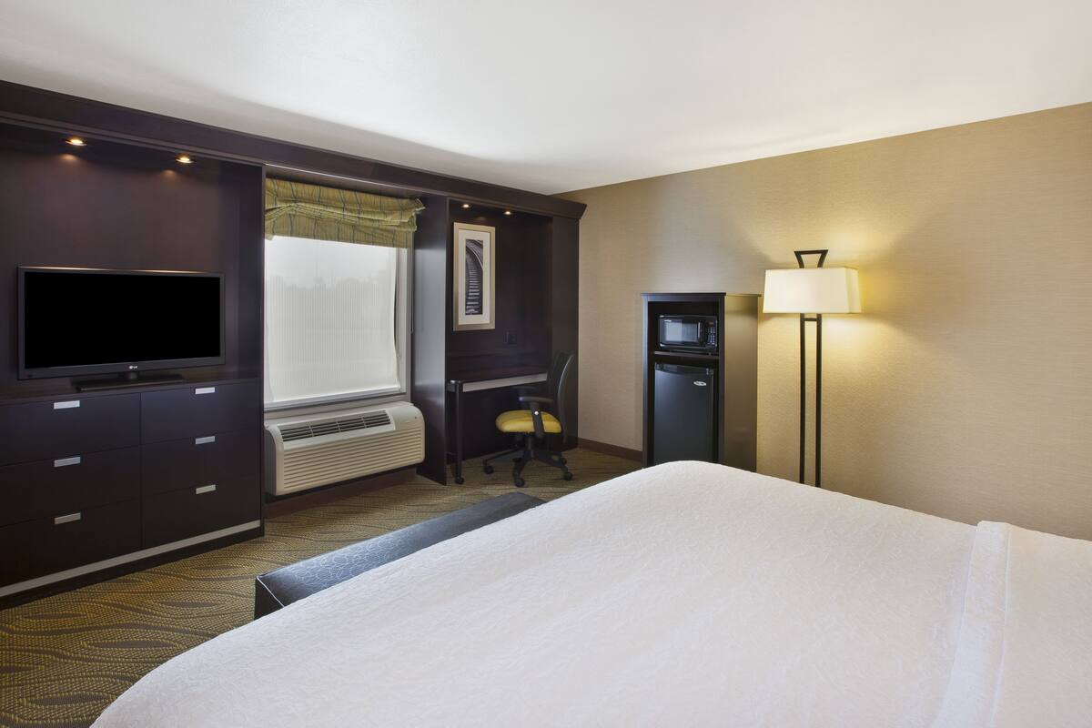 A hotel room with a bed, a desk with a chair, a television, a microwave, and a lamp.