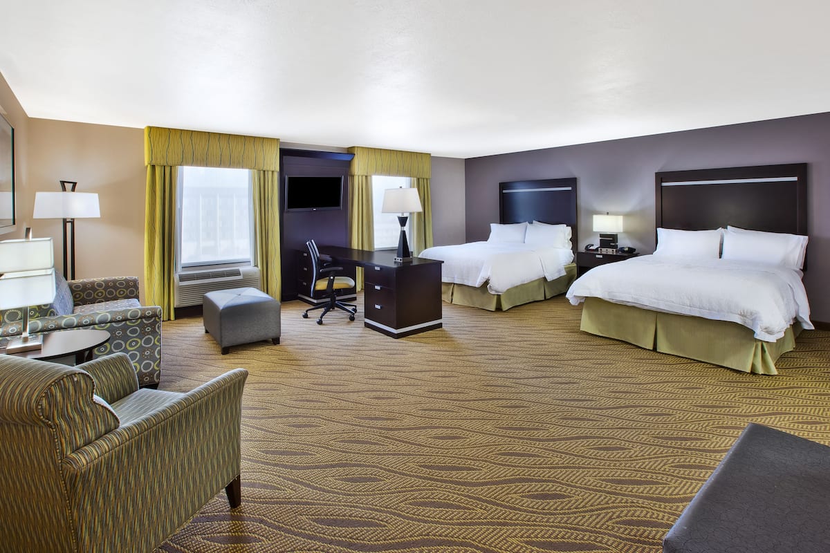 A hotel room with a large bed, a smaller bed, a desk, a chair, a sofa, and a TV.