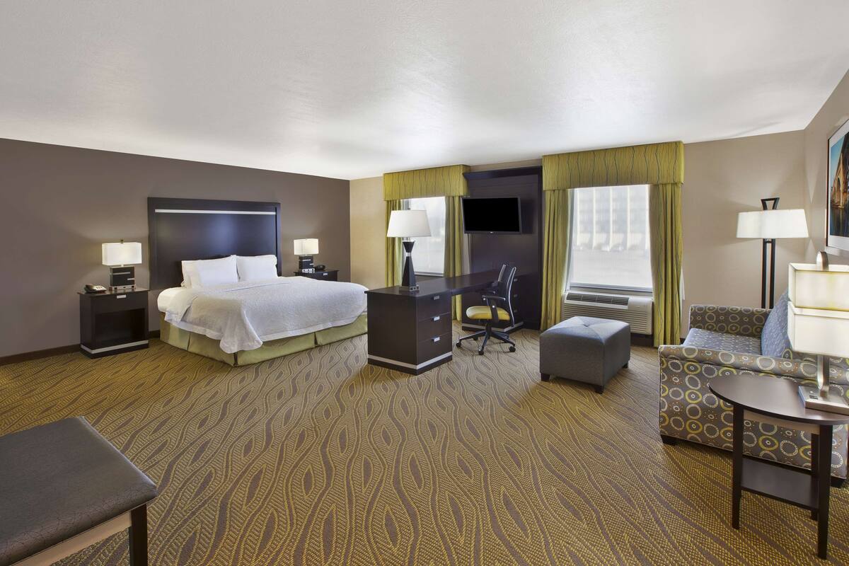 A hotel room with a bed, desk, chair, and ottoman.