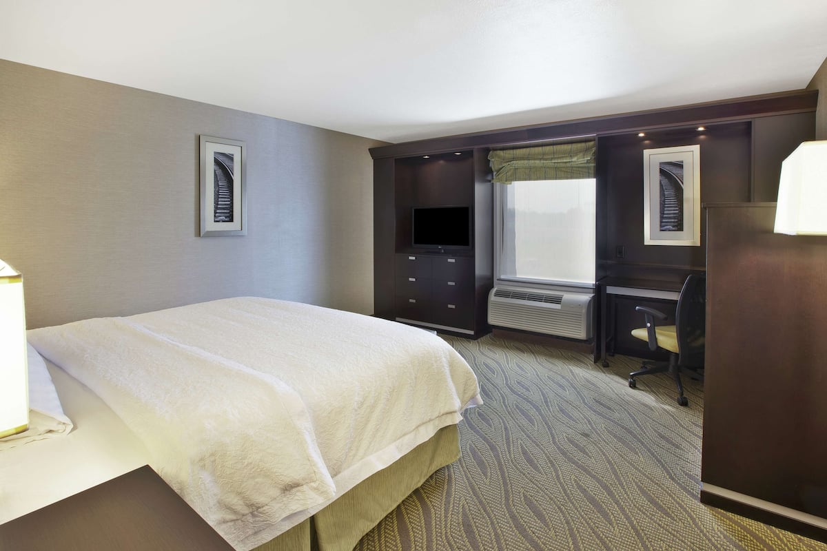 A hotel room with a bed, a desk, a chair, a television, and an air conditioning unit.