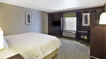 Habitación de hotel con cama, escritorio, silla, televisor y aire acondicionado.