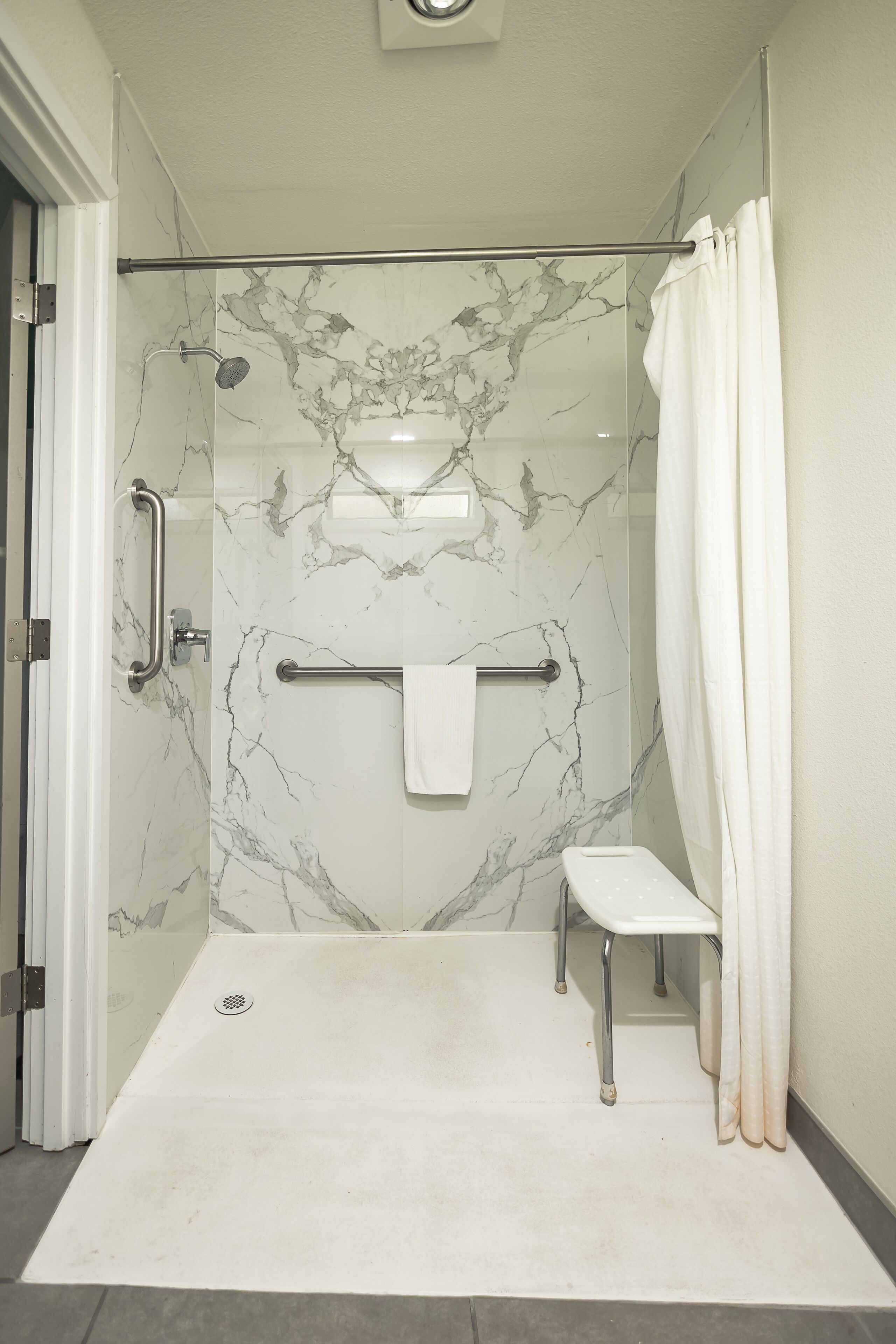 A modern bathroom with a glass-enclosed shower, marble walls, a white bench, and a towel rack.