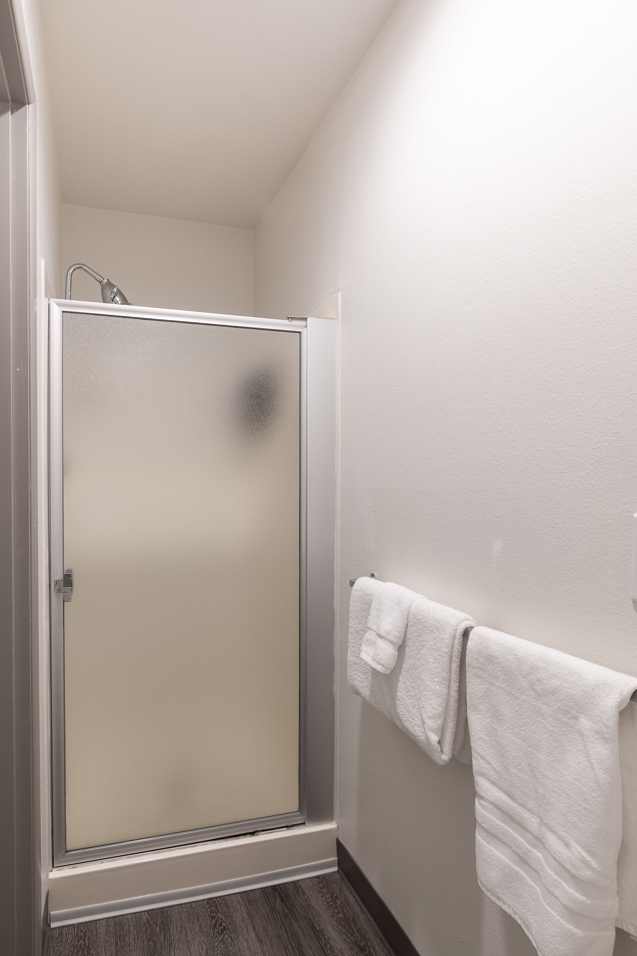 A shower with frosted glass doors, a white towel hanging on the wall, and a wooden floor.