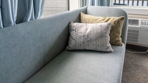 A room with a sofa, a window with curtains, and a view of a bridge and landscape. - Jot's Resort (Gold Beach)