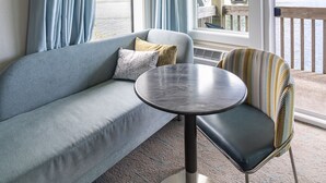 A room with a sofa, a round table, and a view of a bridge and water. - Jot's Resort (Gold Beach)