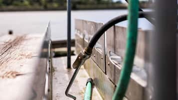 A metal railing with a green hose attached, overlooking a body of water and greenery.