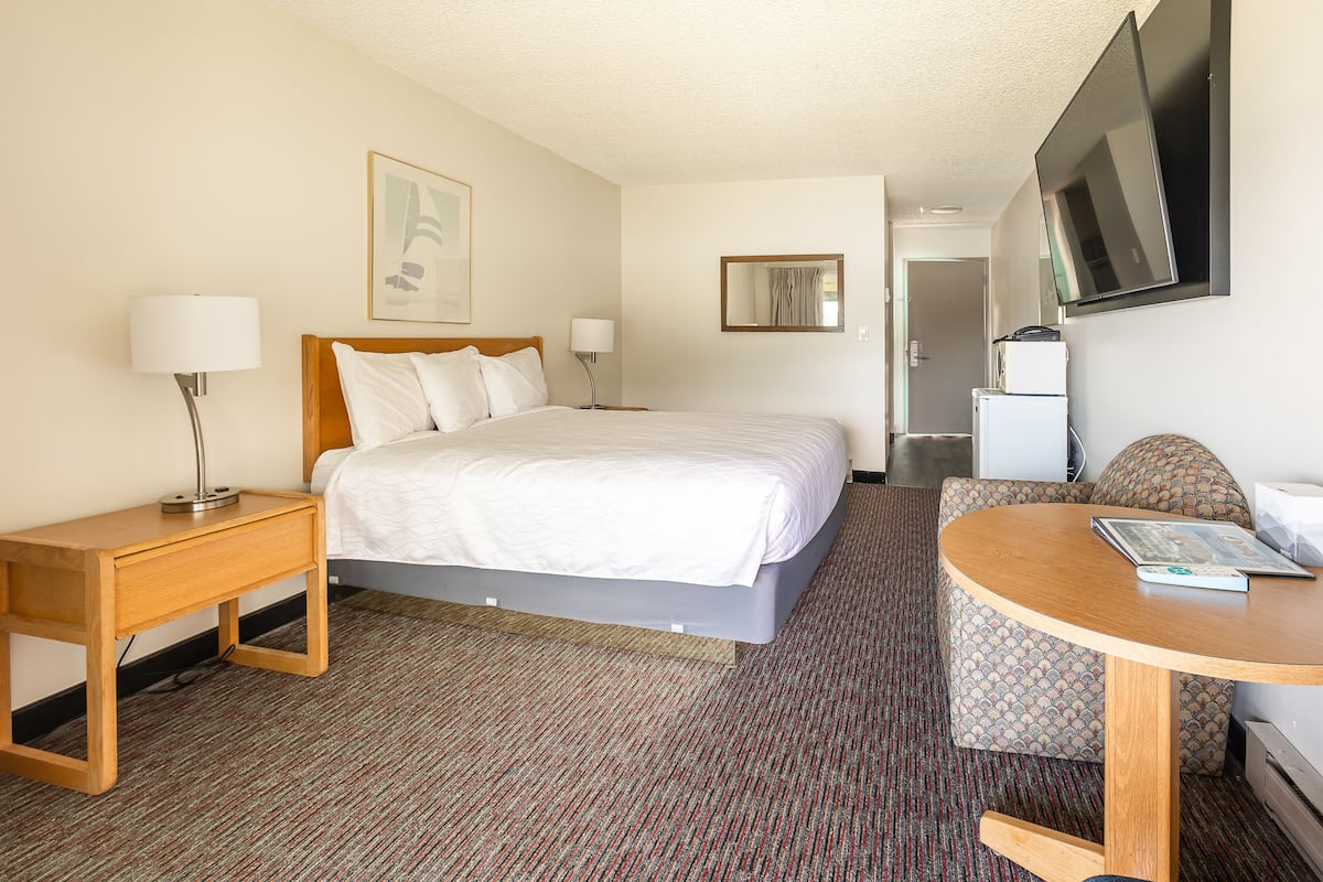 A hotel room with a bed, a desk, a chair, a TV, and a refrigerator.