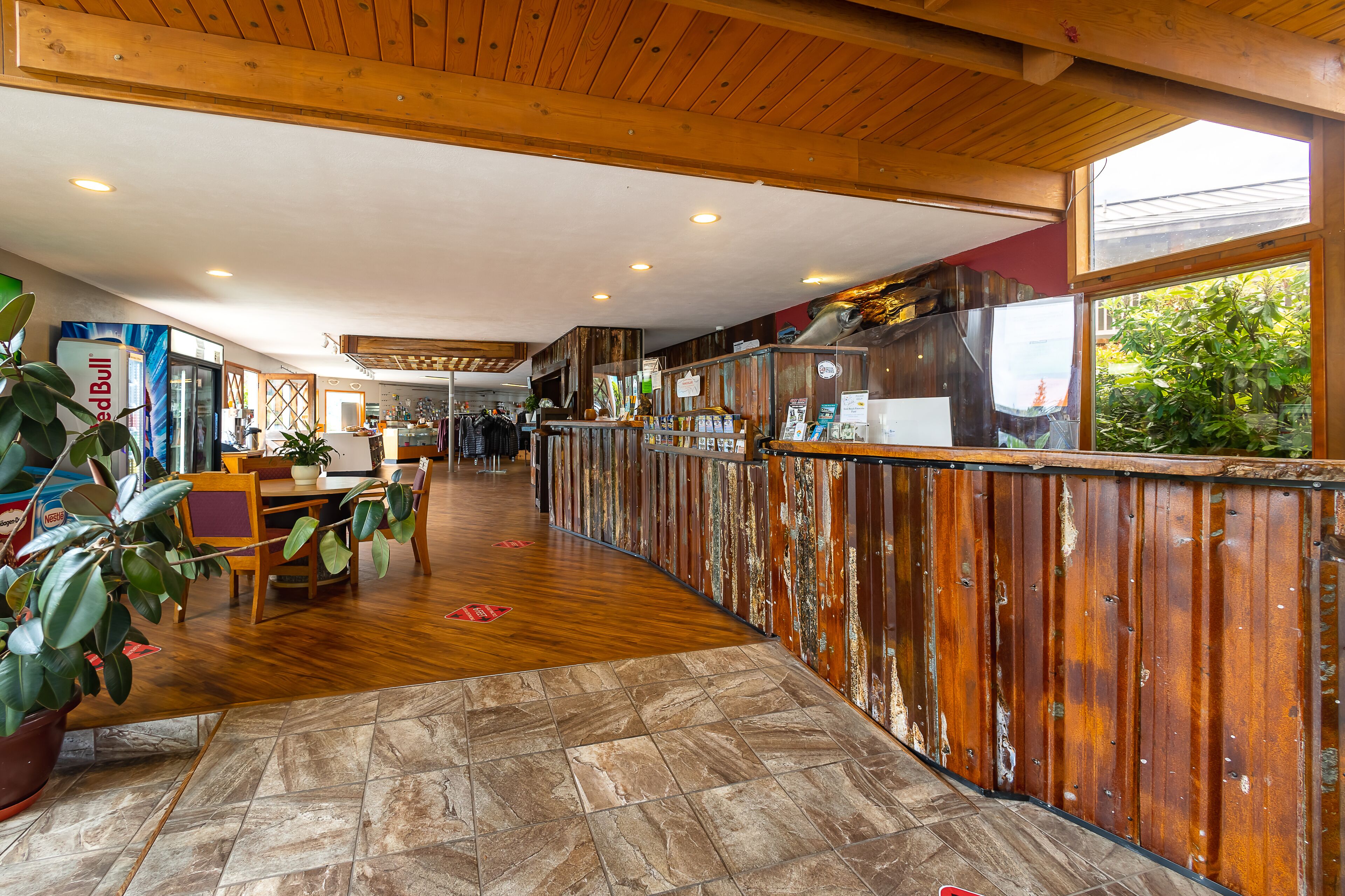 Un hall d’entrée spacieux, doté d’un plancher en bois, d’un comptoir de réception et offrant une vue sur l’extérieur grâce à de grandes fenêtres.