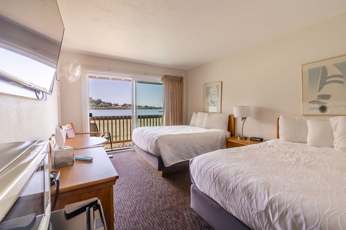 A hotel room with two beds, a desk, a phone, and a window with a view of the sea.