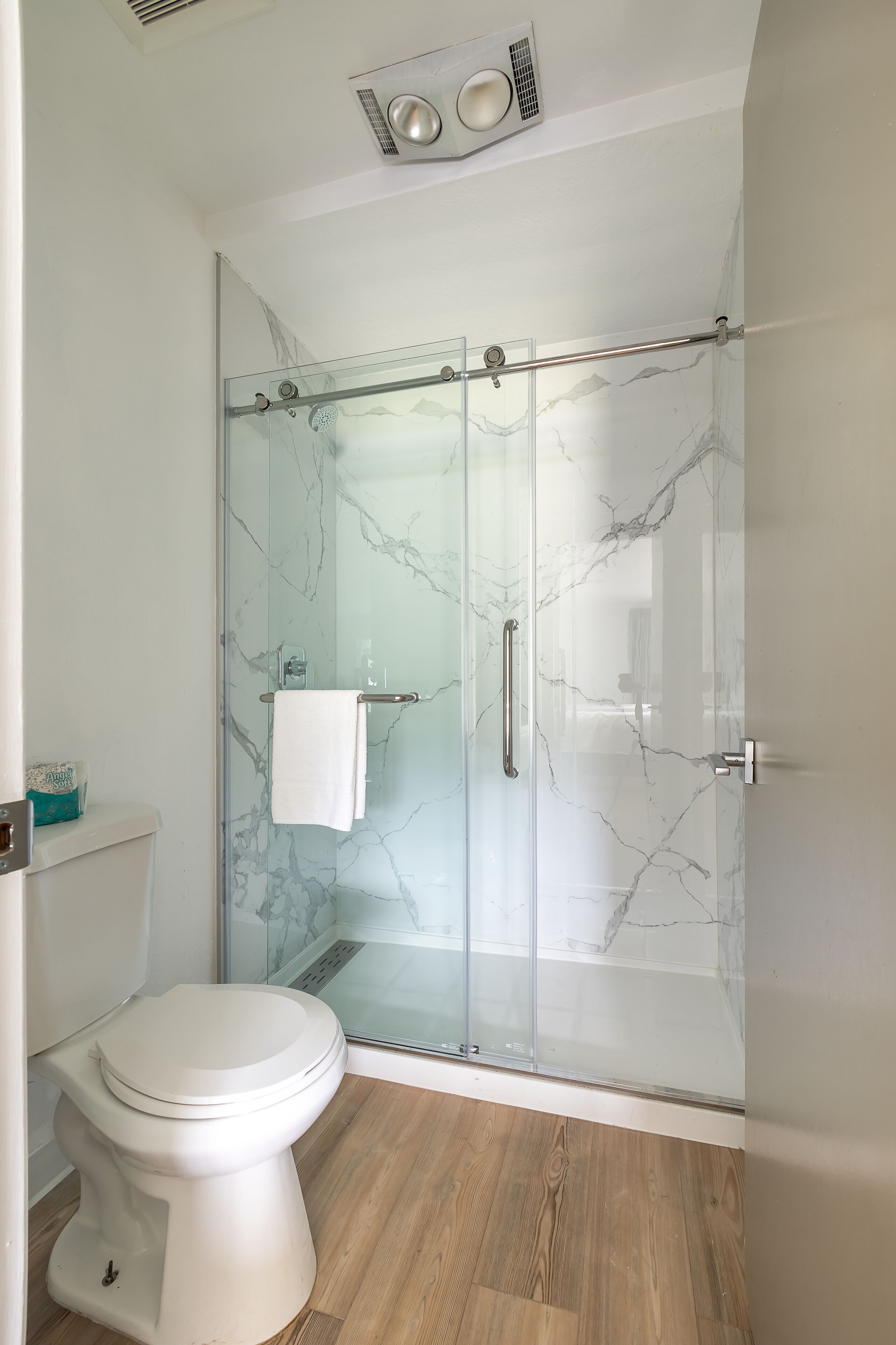 Une salle de bain moderne avec une douche à parois de verre, des toilettes blanches et un pare-baignoire en marbre.